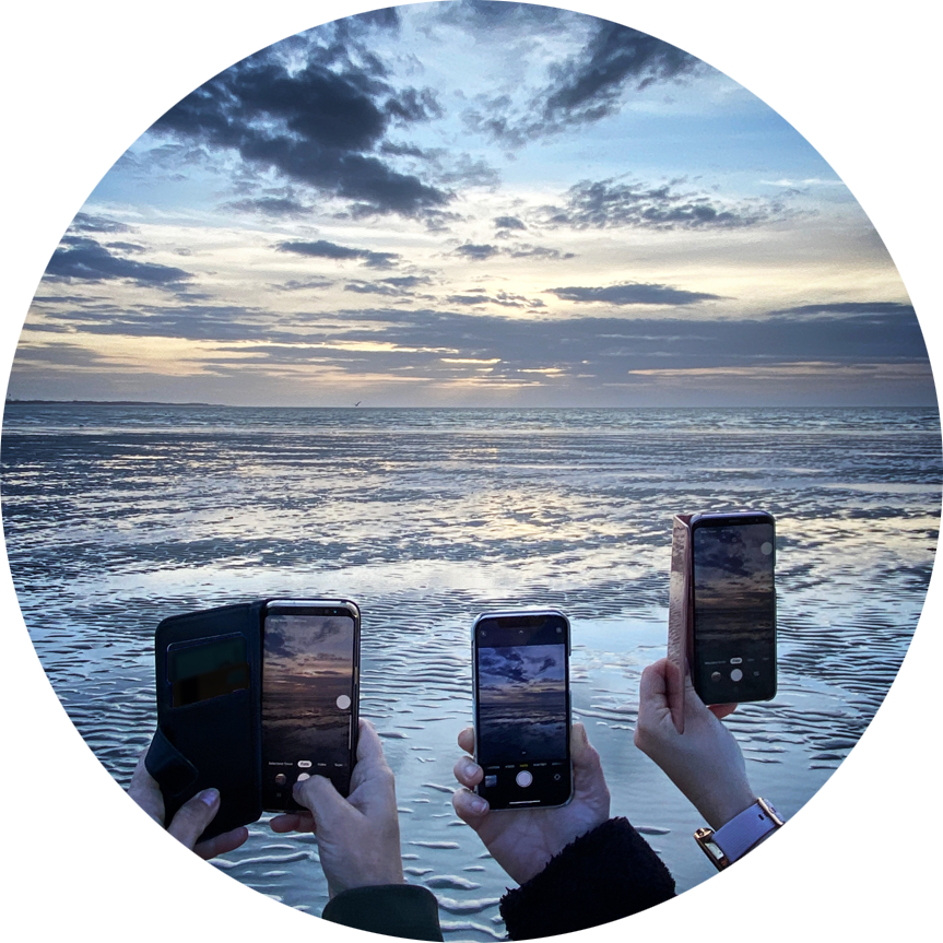 Drie deelnemers maken foto met smartphone van de zee