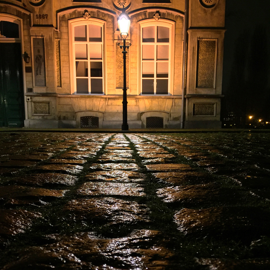 Oud gebouw van voren gefotografeerd in de nacht, met straatverlichting en natte straat