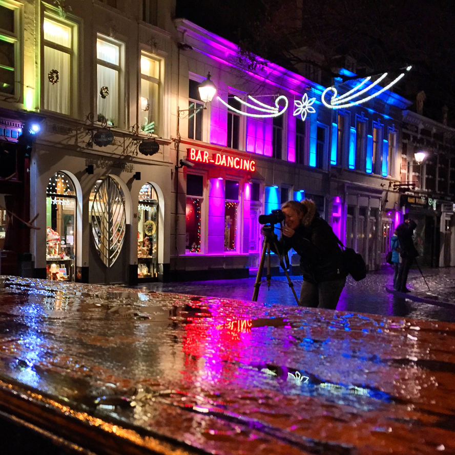 Vrouw fotografeert natte terrastafel en straat in de nacht in neonkleuren licht