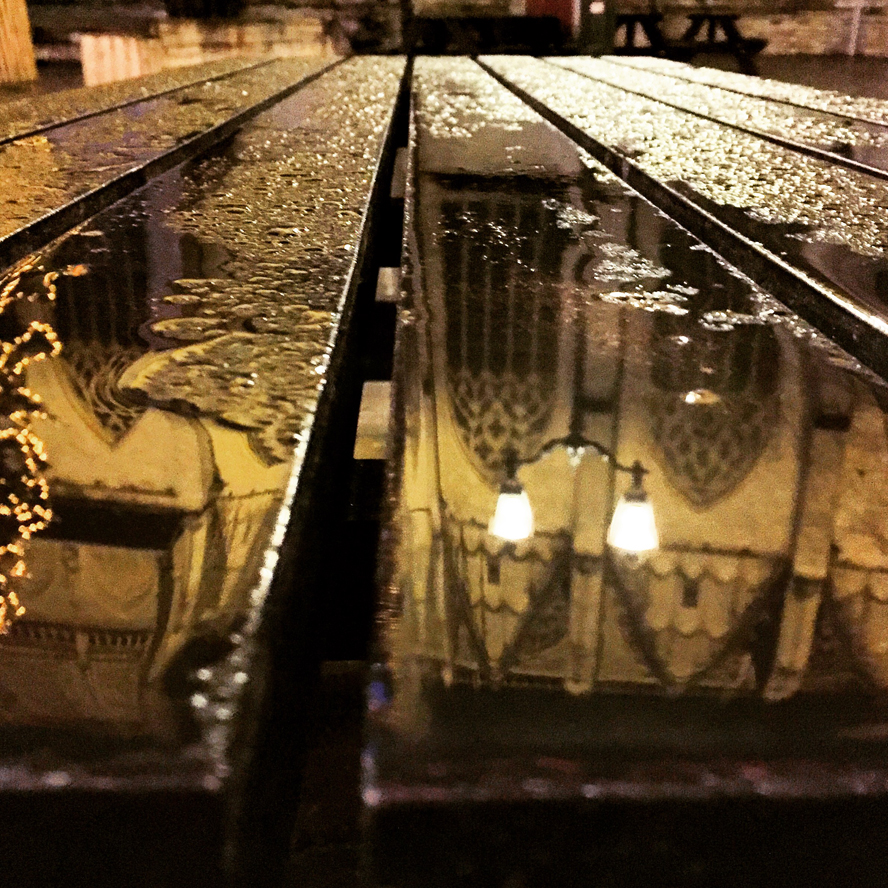 Straatlantaarns reflecteren in een natte terrastafel in de nacht