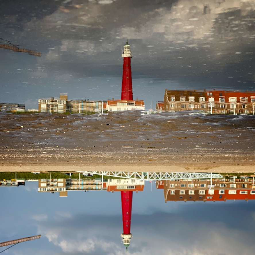 Vuurtoren van Scheveningen op z'n kop in weerspiegeling van water op het strand
