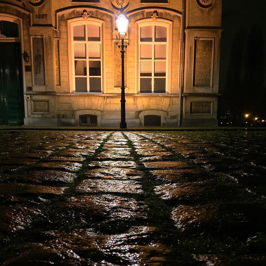 Natte straat met kinderkopjes verlicht door een lantaarnpaal bij nacht