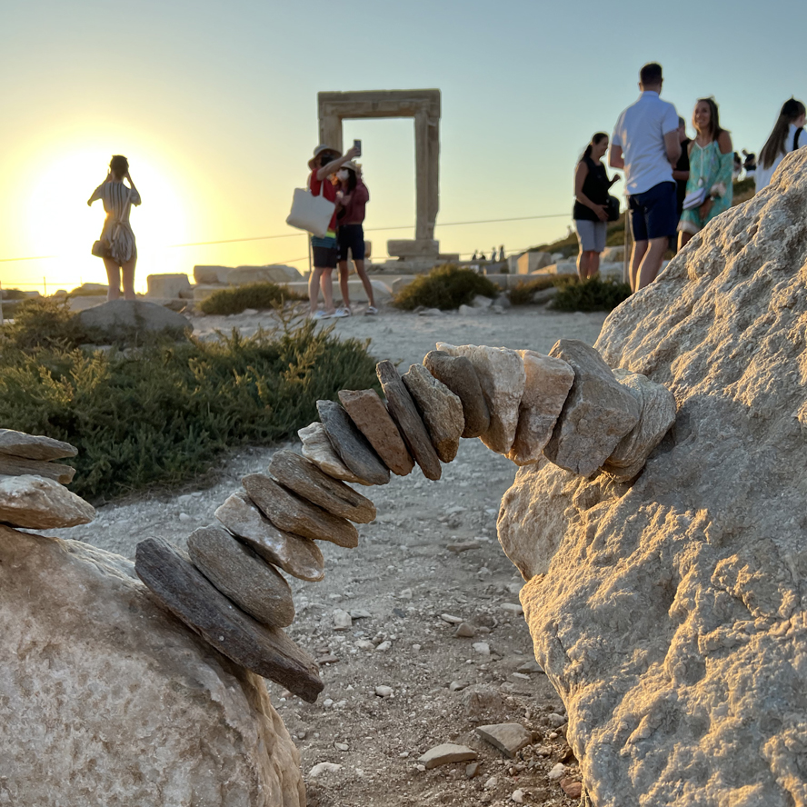 Portara van Apollo op Naxos in avondlicht, mensen op achtergrond en stenen boogje op de voorgrond